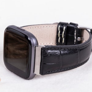 May include: A black leather watch band with a crocodile pattern. The band has a silver buckle and is designed for a smartwatch.