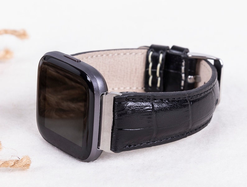May include: A black leather watch band with a crocodile pattern. The band has a silver buckle and is designed for a smartwatch.