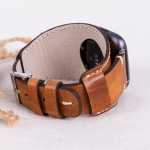 May include: A brown leather watch strap with white stitching and a silver buckle. The strap is designed for a smartwatch and has a loop to secure the strap.