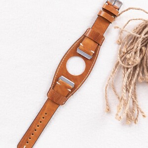 May include: A brown leather watch strap with white stitching and silver buckles. The strap has a unique design with a hole in the middle for a watch face.