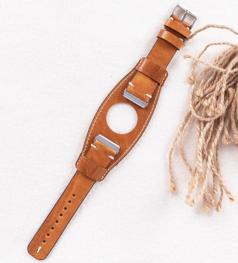 May include: A brown leather watch strap with white stitching and silver buckles. The strap has a unique design with a hole in the middle for a watch face.