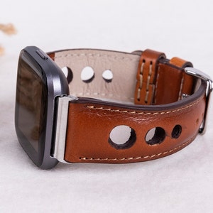May include: A brown leather watch band with a silver buckle and a gray smartwatch. The band has a perforated design with round holes.