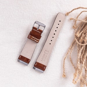 May include: Two brown leather watch straps with white stitching. The strap on the left has a silver buckle. The strap on the right has the text "Full Grain Leather" printed on it.
