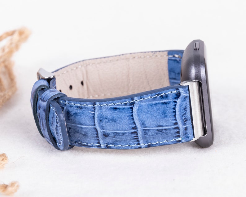 Puede incluir: Una correa de reloj de cuero azul con un patr&oacute;n de cocodrilo. La correa est&aacute; unida a una esfera de reloj plateada.