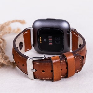 May include: A brown leather watch band with a silver buckle. The band is designed for a smartwatch with a square face.