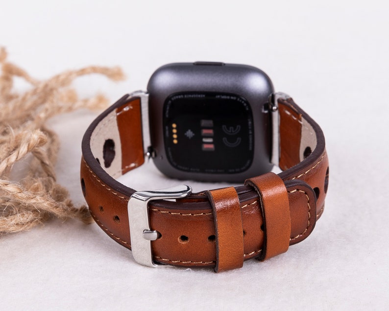 May include: A brown leather watch band with a silver buckle. The band is designed for a smartwatch with a square face.