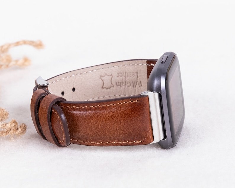 May include: A brown leather watch band with silver hardware and the text "Full Grain Leather" on the inside.