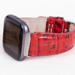 May include: Red leather watch band with a crocodile pattern. The band is attached to a silver watch face.