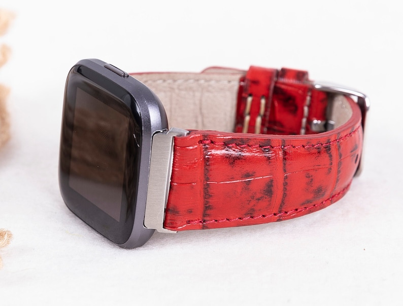 May include: Red leather watch band with a crocodile pattern. The band is attached to a silver watch face.