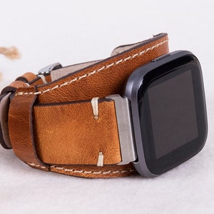 May include: A brown leather watch strap with white stitching. The strap is designed to fit a square-shaped smartwatch.