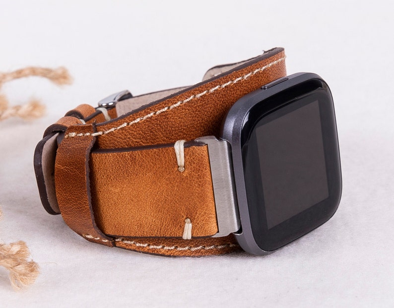 May include: A brown leather watch strap with white stitching. The strap is designed to fit a square-shaped smartwatch.