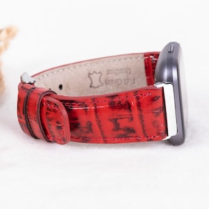 May include: Red leather watch band with a crocodile pattern. The band is made of full grain leather and has a silver buckle.