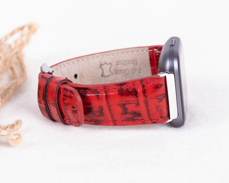 May include: Red leather watch band with a crocodile pattern. The band is made of full grain leather and has a silver buckle.