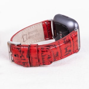 May include: Red leather watch band with a crocodile pattern. The band is made of genuine leather and has a silver buckle. The band is compatible with Fitbit watches.