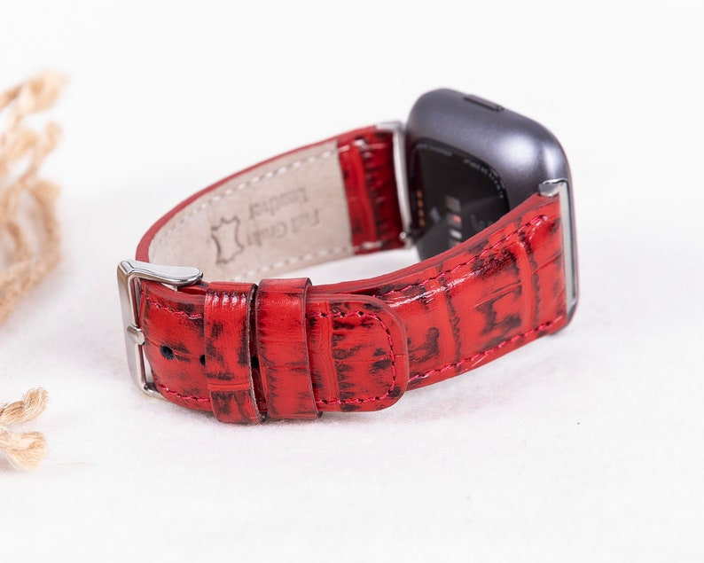 May include: Red leather watch band with a crocodile pattern. The band is made of genuine leather and has a silver buckle. The band is compatible with Fitbit watches.