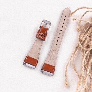 May include: Two brown leather watch straps with silver buckles. The strap on the left has a stitched design. The strap on the right has the text "Full Grain Leather" embossed on it.