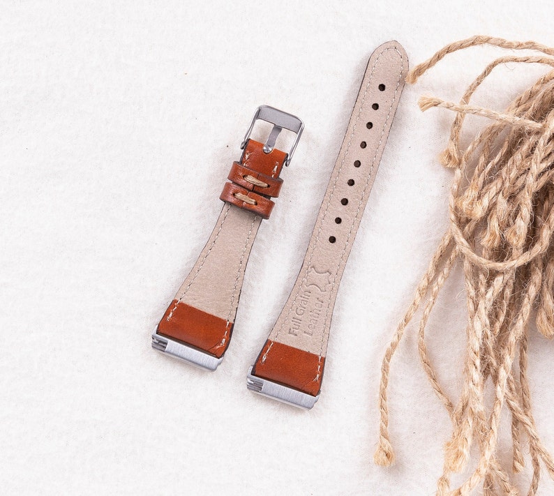 May include: Two brown leather watch straps with silver buckles. The strap on the left has a stitched design. The strap on the right has the text "Full Grain Leather" embossed on it.