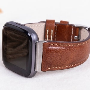 May include: A brown leather watch band with a silver buckle and a black smartwatch face.