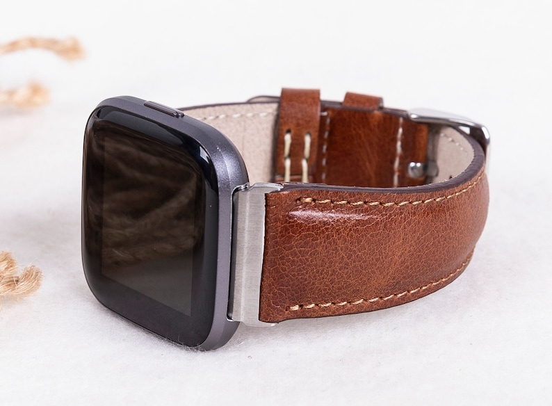 May include: A brown leather watch band with a silver buckle and a black smartwatch face.