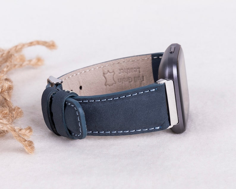 May include: A dark blue leather watch band with white stitching and a silver buckle. The band is labeled "Full Grain Leather".