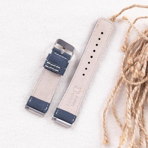 May include: A dark blue leather watch strap with white stitching and silver hardware. The strap is made of full grain leather and has a "Full Grain Leather" label on the back.