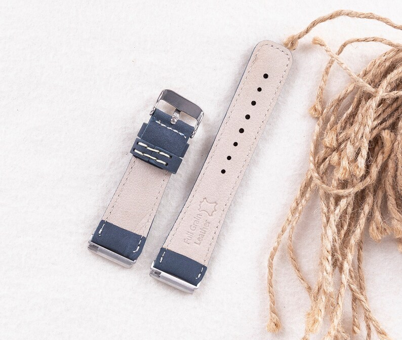 May include: A dark blue leather watch strap with white stitching and silver hardware. The strap is made of full grain leather and has a "Full Grain Leather" label on the back.