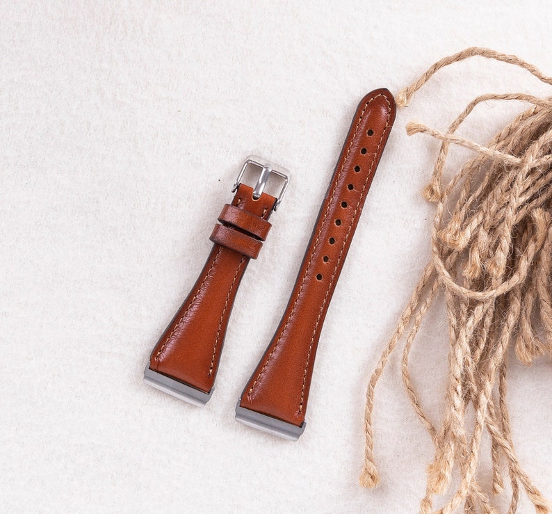 May include: Two brown leather watch straps with silver buckles. The straps are on a white surface.