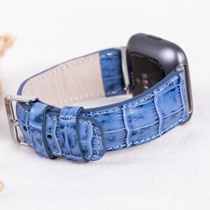 Puede incluir: Una correa de reloj de cuero azul claro con un patr&oacute;n de cocodrilo. La correa est&aacute; dise&ntilde;ada para un reloj inteligente con una cara cuadrada.