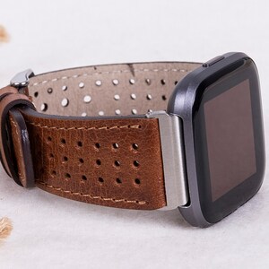 May include: A brown leather watch band with a perforated design. The band is attached to a silver watch face with a black screen.