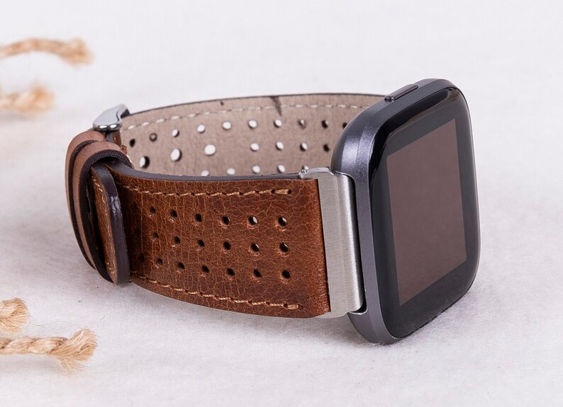 May include: A brown leather watch band with a perforated design. The band is attached to a silver watch face with a black screen.