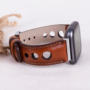 May include: A brown leather watch band with a silver buckle and a smartwatch attached. The band has a perforated design.