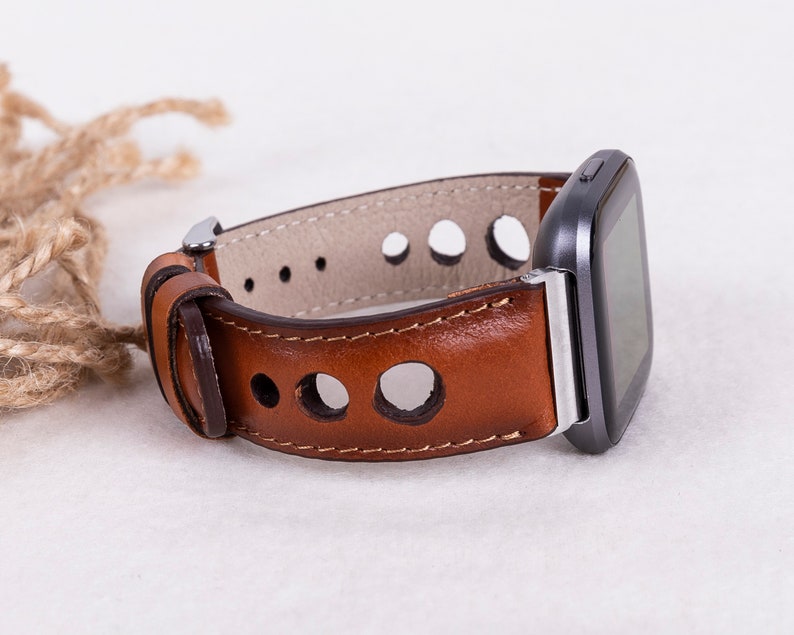 May include: A brown leather watch band with a silver buckle and a smartwatch attached. The band has a perforated design.