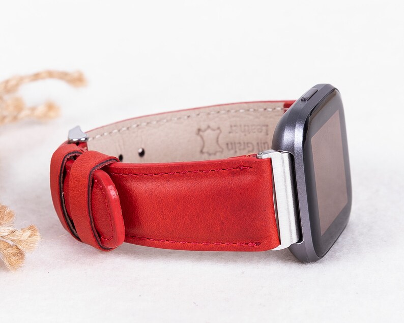 Puede incluir: Correa de reloj de cuero rojo con hebilla plateada. La correa est&aacute; hecha de cuero genuino y tiene un acabado liso. La correa es compatible con los relojes inteligentes Fitbit Versa.