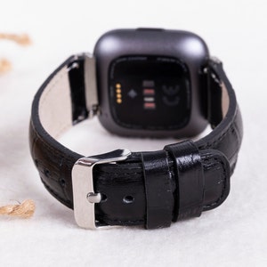May include: Black leather watch band with a silver buckle and a silver watch face. The watch face has a black background and a small white display with four dots and a line.