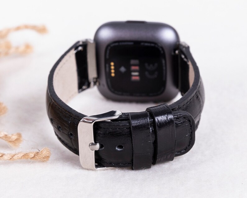 May include: Black leather watch band with a silver buckle and a silver watch face. The watch face has a black background and a small white display with four dots and a line.