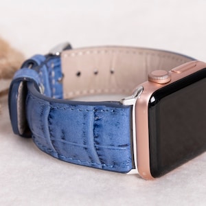 May include: A blue leather watch strap with a rose gold Apple Watch.