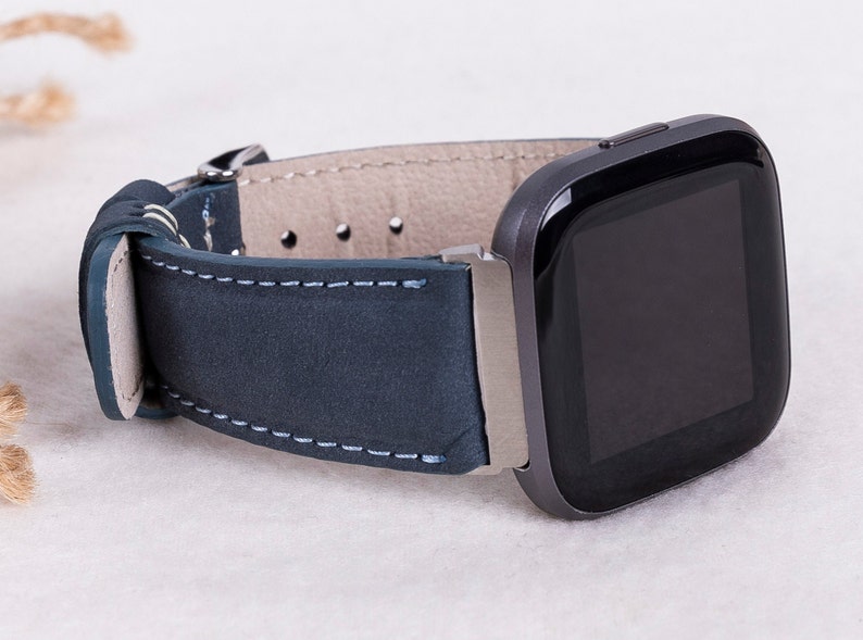 May include: A dark blue leather watch band with white stitching, attached to a black smartwatch with a square face.