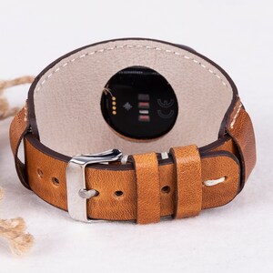 May include: A brown leather watch strap with white stitching and a silver buckle. The strap is designed to fit a smartwatch with a round face.