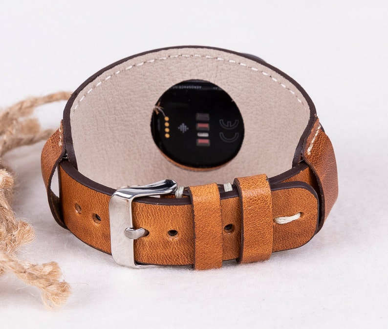 May include: A brown leather watch strap with white stitching and a silver buckle. The strap is designed to fit a smartwatch with a round face.