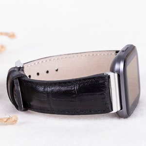 May include: A black leather watch band with a silver buckle and a gray smartwatch.