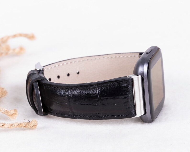 May include: A black leather watch band with a silver buckle and a gray smartwatch.