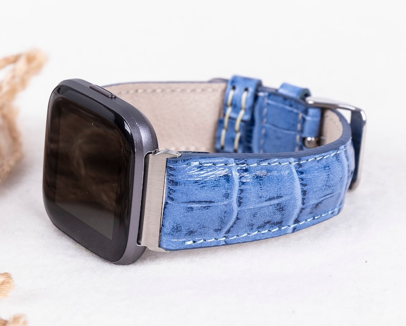 Puede incluir: Una correa de reloj de cuero azul con un patr&oacute;n de cocodrilo. La correa est&aacute; dise&ntilde;ada para un reloj inteligente con una cara cuadrada.