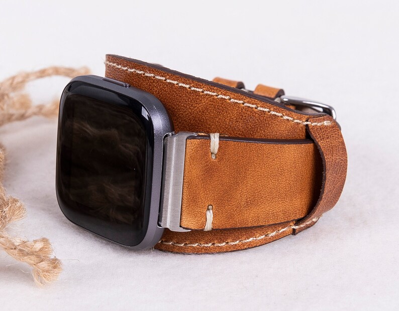 May include: A brown leather watch strap with white stitching. The strap is designed to fit a square-shaped smartwatch.