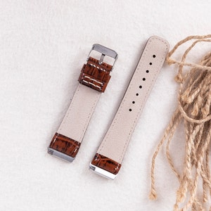 May include: Two brown leather watch straps with silver buckles. The straps have a crocodile pattern and are laid out on a white surface.