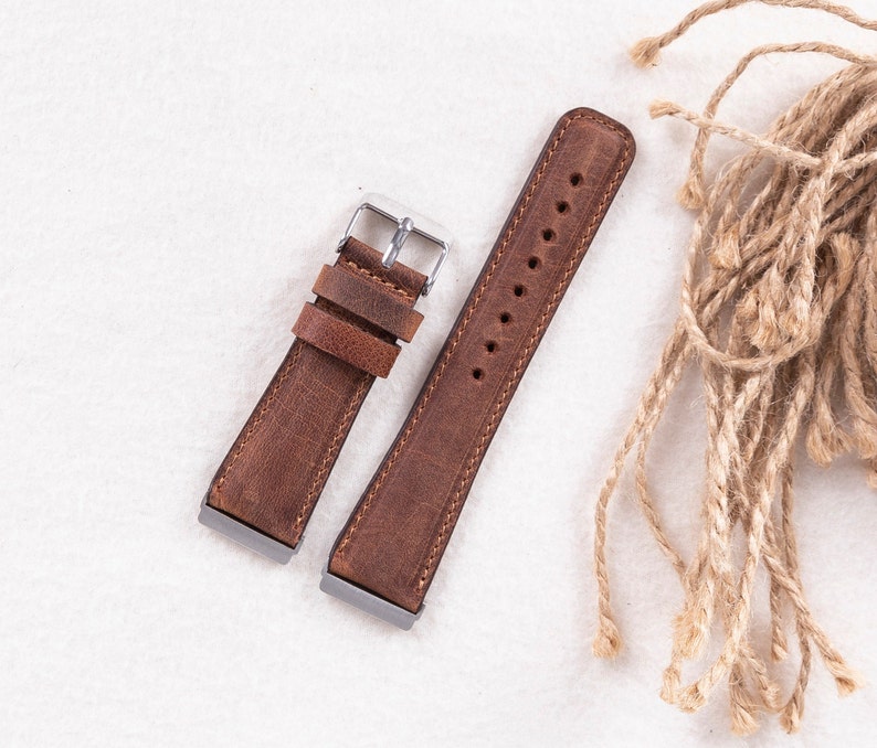 Puede incluir: Dos correas de reloj de cuero marr&oacute;n con hebillas plateadas. Las correas est&aacute;n dispuestas sobre una superficie blanca.