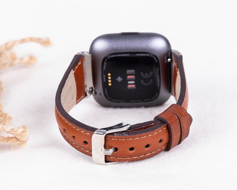 May include: A brown leather watch strap with a silver buckle and a silver smartwatch with a black screen and the CE mark.