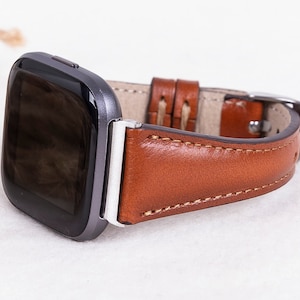 May include: A brown leather watch strap with white stitching. The strap is attached to a silver watch with a black face.