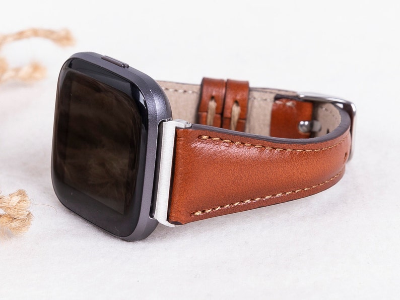 May include: A brown leather watch strap with white stitching. The strap is attached to a silver watch with a black face.