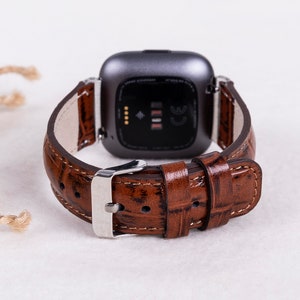 May include: A brown leather watch band with a crocodile pattern. The band is attached to a silver watch with a black face.