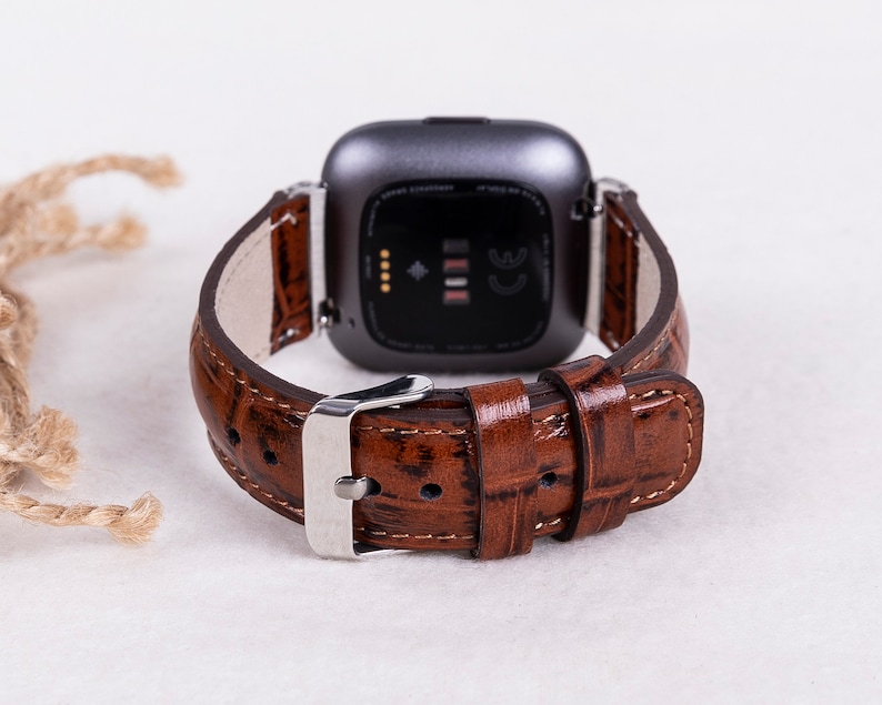 May include: A brown leather watch band with a crocodile pattern. The band is attached to a silver watch with a black face.